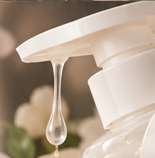 Close-up of an ivory-colored pump dispenser with a hanging droplet against a warm, soft-focus background
