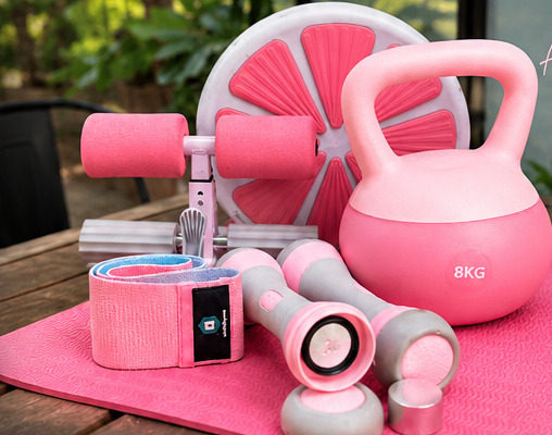 Pink kettlebell, dumbbells, ab roller, resistance band and exercise mat arranged on a wooden outdoor table