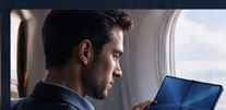 Traveler working with a foldable device beside an airplane window.